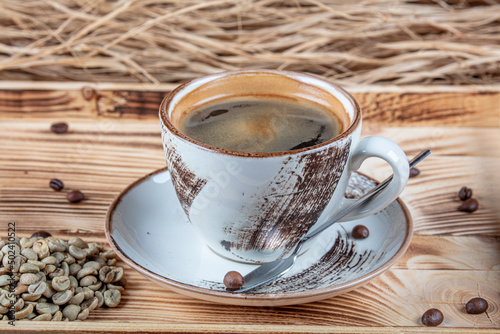 Hot coffee in a coffee cup and many coffee beans are placed around it, on a wooden table in a warm, light atmosphere, on dark background, with copy space.