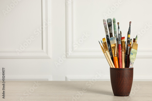 Different paintbrushes in holder on white wooden table. Space for text