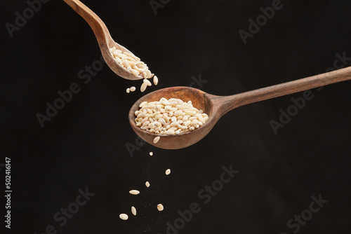  Falling pearl barley grains from a small spoon into a big wooden spoon a black background. Shallow depth of field