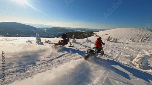 A sunlight aerial top view in mountains, two guy on snowmobile jumps and rides in the winter. Beautiful landscape