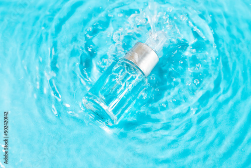 Bottle serum or cosmetic oil in clean transparent water with sunlight on blue background, flat lay, top view, copy space. Cosmetic spa medical skin care concept.