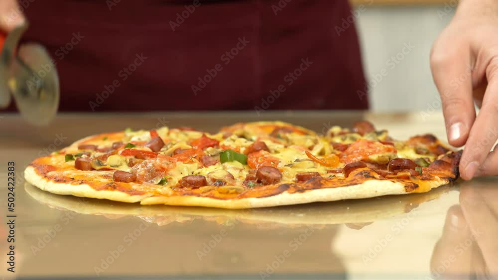 Man slicing pizza with a round knife, close view. Person cutting a pizza into multiple slices with a cutter on glossy reflecting table. Man slicing pizza with a round knife, close view. Person cutting a pizza into multiple slices with a cutter on glossy reflecting table.