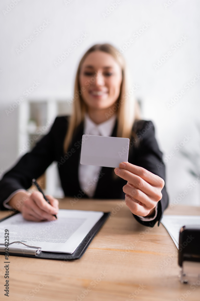 smiling notary holding blank business card on blurred background. smiling notary holding blank business card on blurred background.