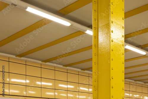 Closeup of a vertical yellow metal pole with a modern white ceiling in U Weberwiese station, Germany photo