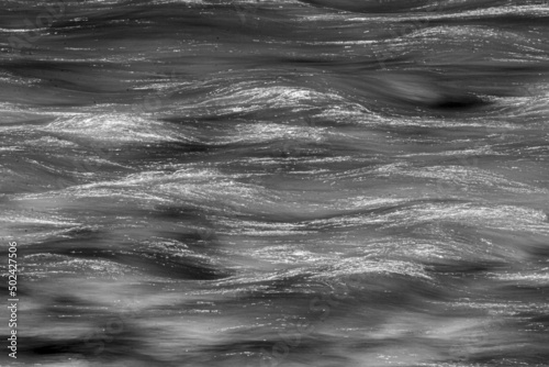 Grayscale of waves flowing water with random shadows on a sunny day