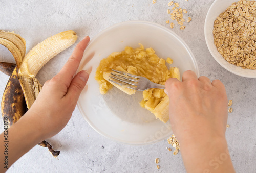 A woman mashes bananas with a fork to bake banana cookies.