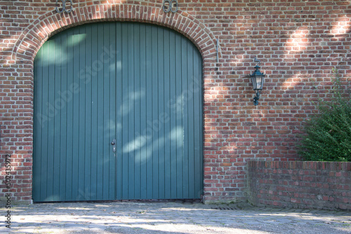 Big blue wooden door in a red bricked building with small lamo posts on the walls photo