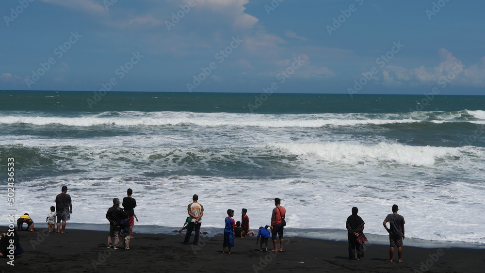 Yogyakarta, Indonesia - may 4 2022 : On a beautiful beach with quite big waves some people are playing, They are quite careful and keep their distance so as not to be dragged by the waves