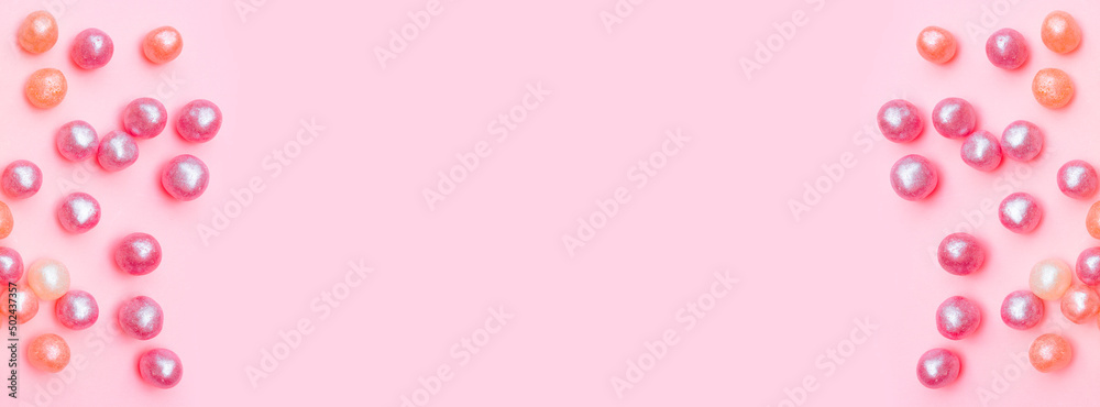 Banner with round candies in glaze. Candy pearls. Orange and purple. Pink Background. Flat lay. Top view. Copy space. Place for text. Holiday invitation. Beautiful sweets. For web design. Banner with round candies in glaze. Candy pearls. Orange and purple. Pink Background. Flat lay. Top view. Copy space. Place for text. Holiday invitation. Beautiful sweets. For web design.