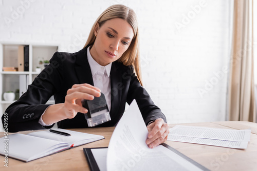 blonde notary holding stamper while working with documents in office. photo