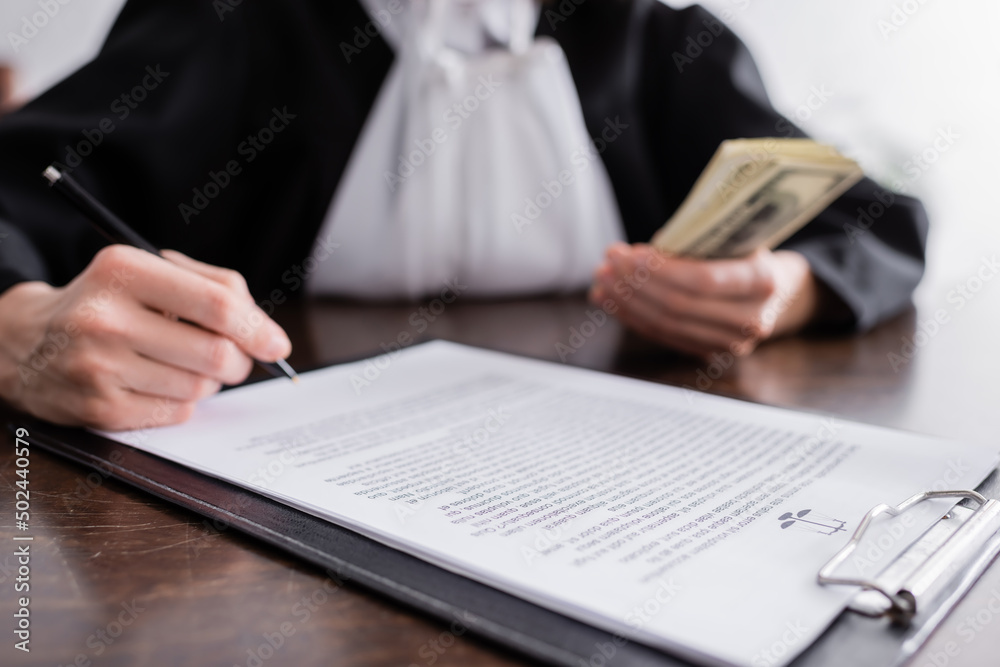 cropped view of blurred prosecutor with pen and money near lawsuit on clipboard. cropped view of blurred prosecutor with pen and money near lawsuit on clipboard.