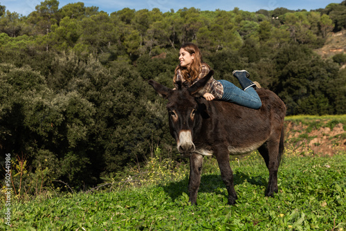 A young woman resting on a donkey looking away in a meadow