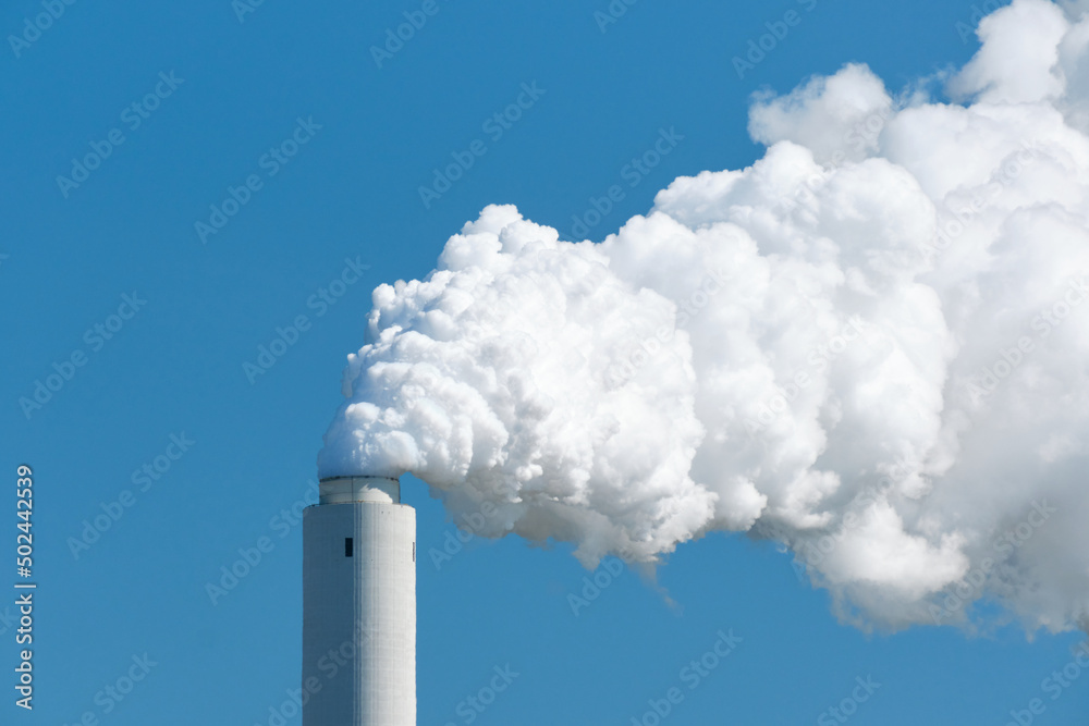 Cooling tower of an active coal power plant with thick steam in front of blue sky Cooling tower of an active coal power plant with thick steam in front of blue sky