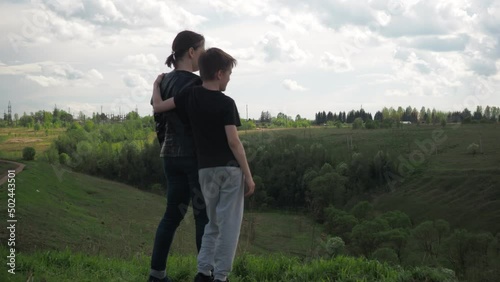 a boy with a young mother on a hill looking into the distance in an embrace. happy family. view from the back