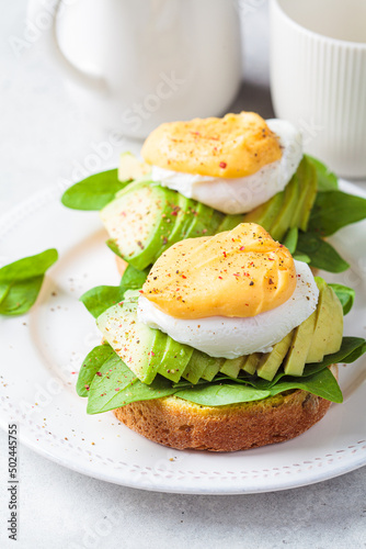 Eggs benedict on bun with spinach, avocado and hollandaise sauce. Delicious vegetarian breakfast concept.