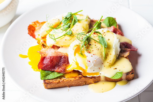 Eggs benedict on crispy toast with bacon and traditional hollandaise sauce. Delicious breakfast concept.