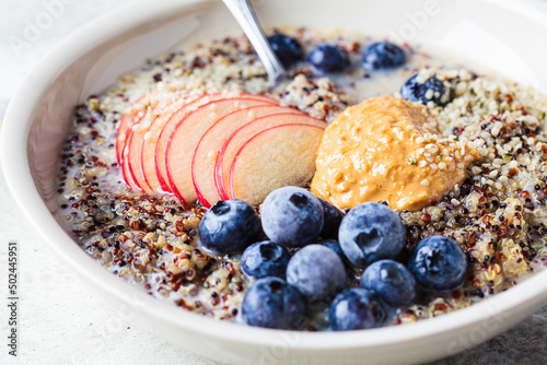 Quinoa porridge with apple, blueberry, peanut butter and hemp seeds for breakfast. Vegan food concept.