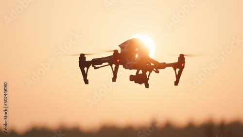 Flying copter black drone monitoring farming fields above rural landscape. Sunset sky. Agriculture and business. Smart technology.