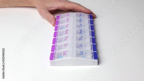 Hand putting vitamin into plastic pill case on white table, close up. photo