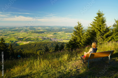 A woman sitting on a bench, looking from mount Hohenbogen to Neukirchen Heiligblut, a small town in the Bavarian Forest. photo