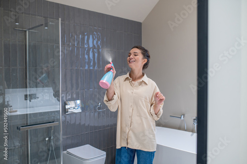 A smiling young woman spraying the air freshener in the bathroom photo