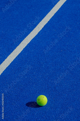 Isolated ball on a blue paddle tennis court, racket sports concept © Vic