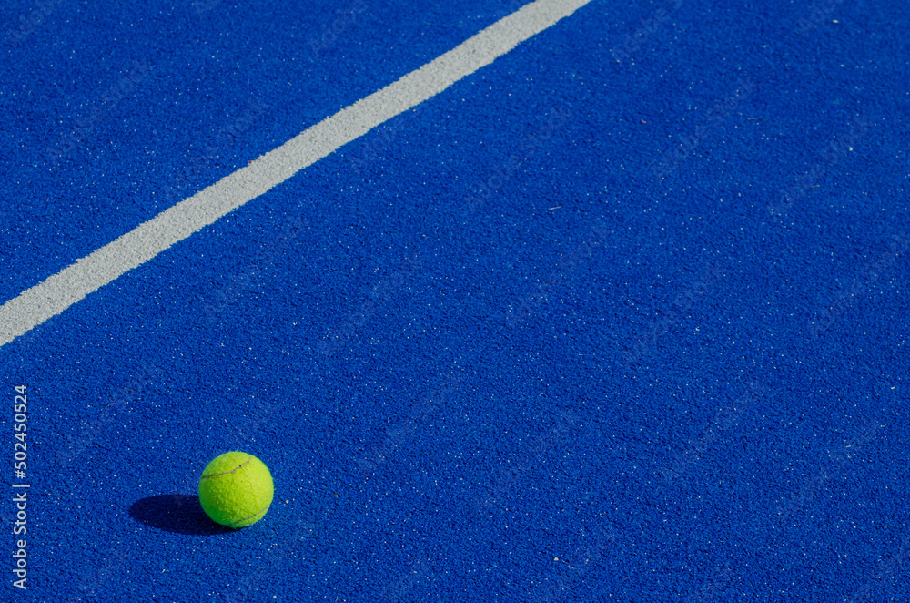Isolated ball on a blue paddle tennis court, racket sports concept