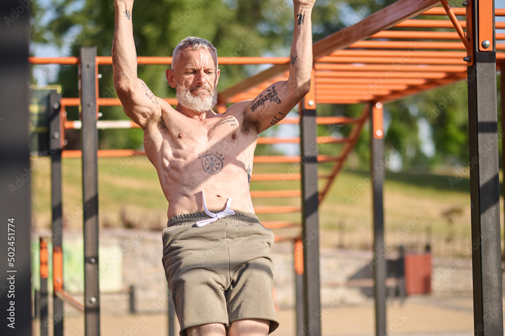 A gray-haired mature man having a workout on the open sports ground