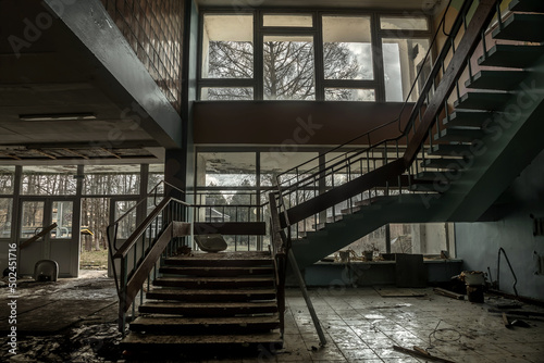 Beautiful dark hall with an old staircase. An old abandoned building. Dirty shabby walls and steps. Large transparent windows. Old creepy abandoned building.