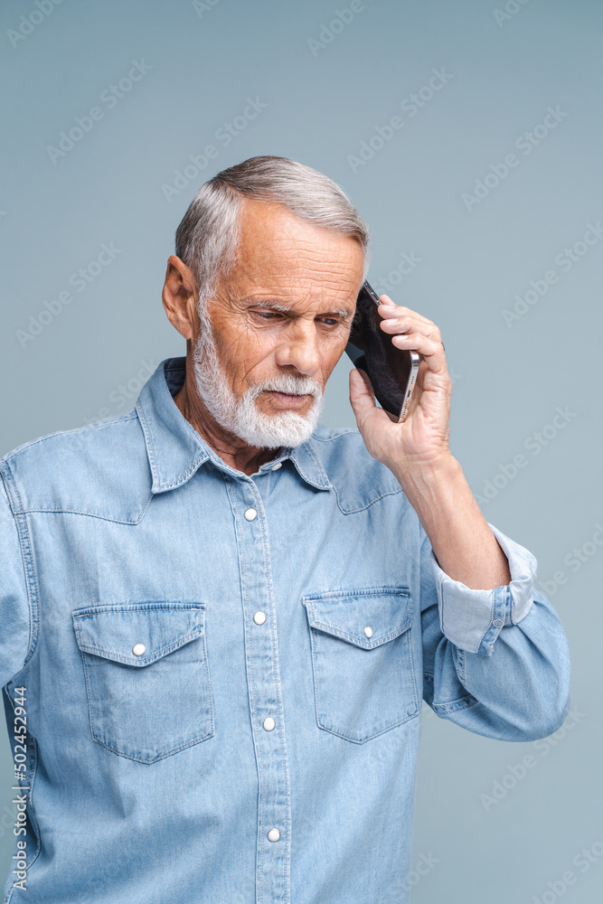Busy retirement man calling to somebody, looking down with concentrated face. Indoor studio shot isolated on blue background Busy retirement man calling to somebody, looking down with concentrated face. Indoor studio shot isolated on blue background