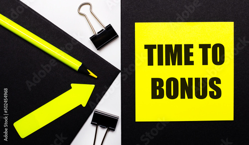 On a black background, a bright yellow pencil and an arrow and a yellow sheet of paper with the text TIME TO BONUS. photo