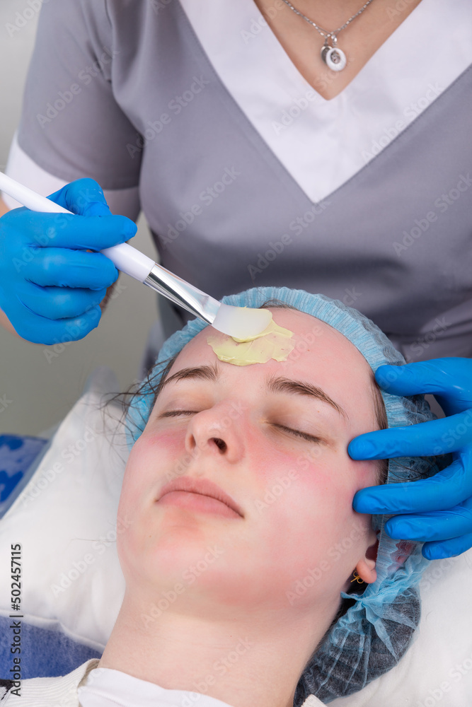 Naklejka premium Cosmetologist applies alginate mask with spatula on face of woman.