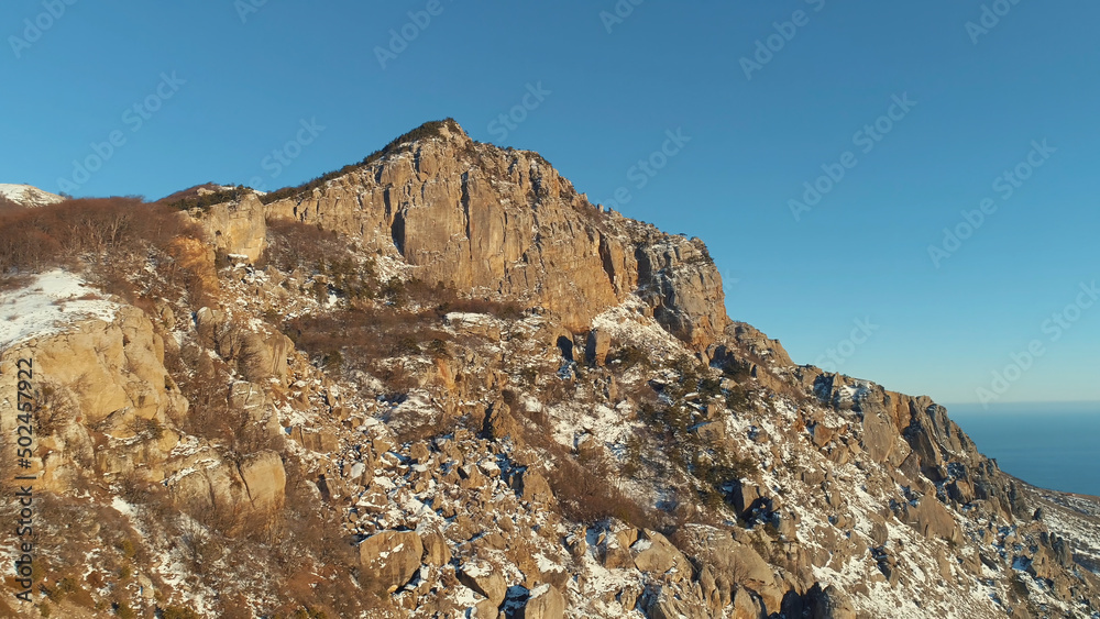 Aerial drone view of mountain range in winter season on blue sky background. Shot. Flying over breathtaking rock formation covered by trees.