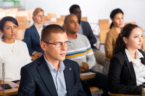 Young confident man sitting and listening speaker at business conference