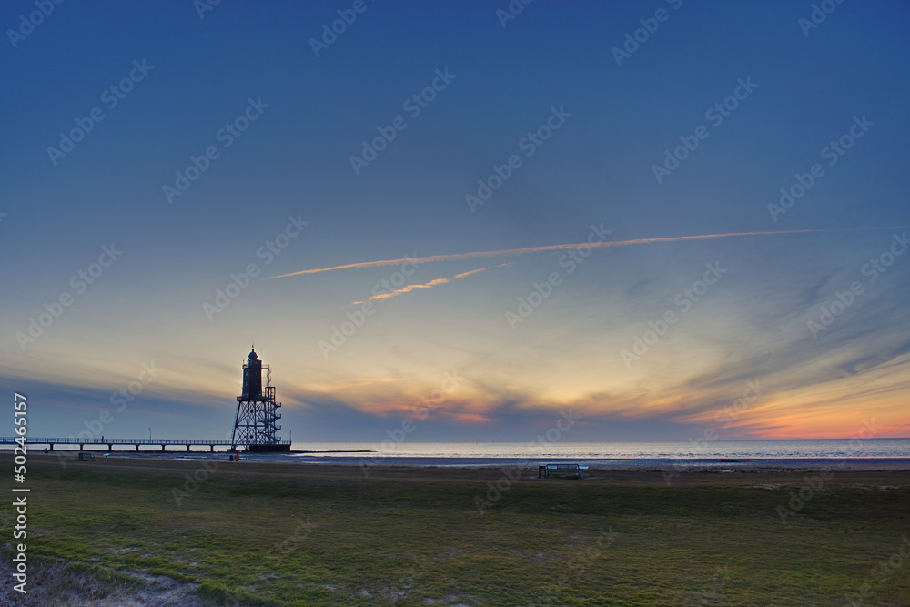 Fototapeta premium sunset at a lighthouse at low tide at north sea coast