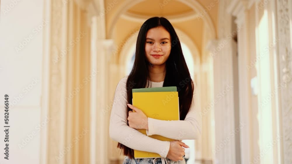Student asian girl in eyeglasses with books walking near the university building. Happy and smiling walking forward. Student asian girl in eyeglasses with books walking near the university building. Happy and smiling walking forward.