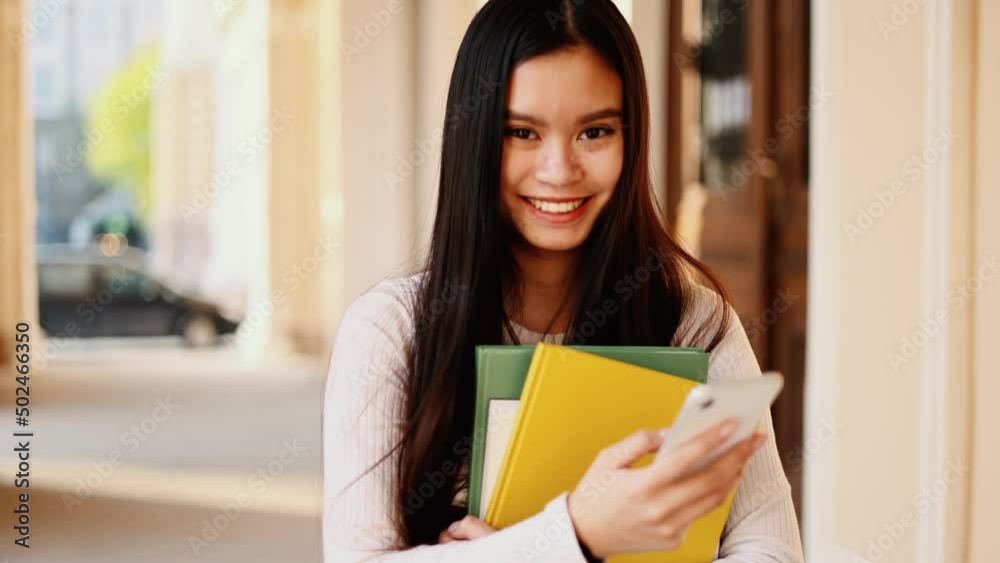 Portrait of attractive student young asian woman walking near the university building hold smartphone, watching social media. Smiling young woman texting on her phone. Portrait of attractive student young asian woman walking near the university building hold smartphone, watching social media. Smiling young woman texting on her phone.