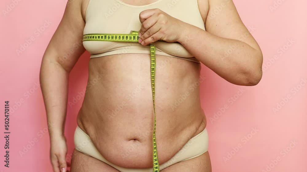 Cropped shot of adipose woman with big cellulite sagging tummy, measuring the circumference of her breast and chest with a tape roulette. Checking size after dieting. Showing off obesity problem body Cropped shot of adipose woman with big cellulite sagging tummy, measuring the circumference of her breast and chest with a tape roulette. Checking size after dieting. Showing off obesity problem body