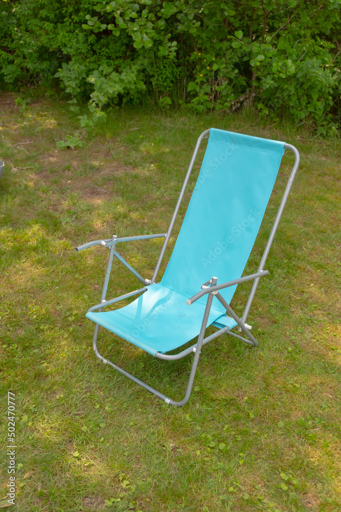 A blue beach chair placed in the shadow in a park..