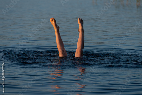 A person standing upside down in a lake. Legs visible over water..