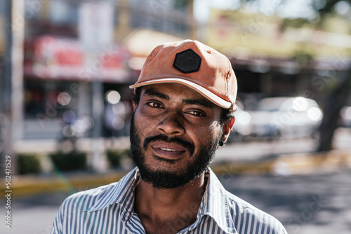 Man in street condition with cap and beard looking at camera. 