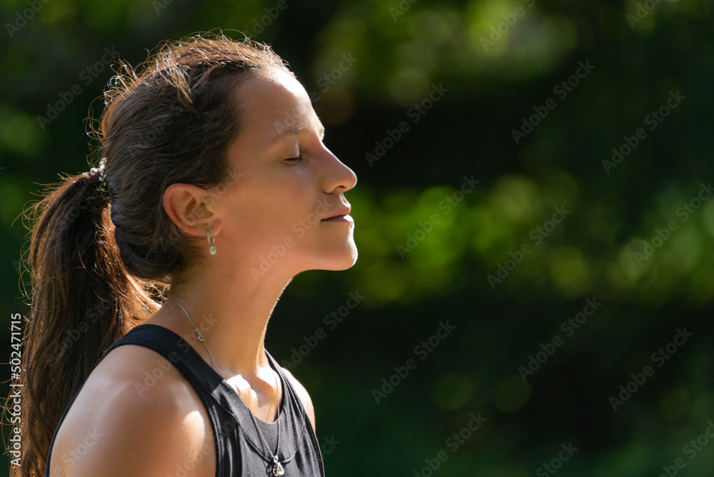 Side View of Young Woman Face Breathing and Enjoying the Sun Against Green Nature Background