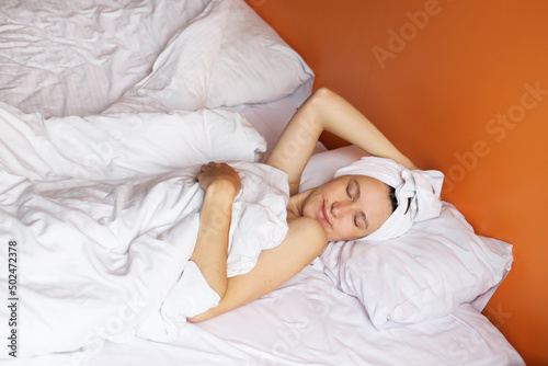 Young girl with clean skin with a towel on her head lying in bed, resting after a shower, relaxing at home.