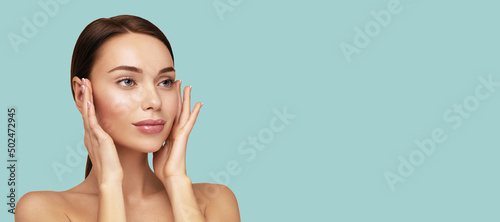 Moisturizing and facial treatment. Beauty portrait of beautiful model with perfect skin touching her face. Web banner with cope space