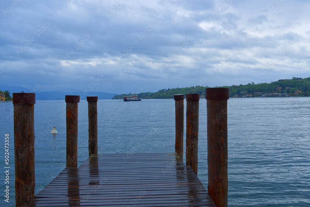 wooden jetty at a lake with ferry in the background in a cloudy day