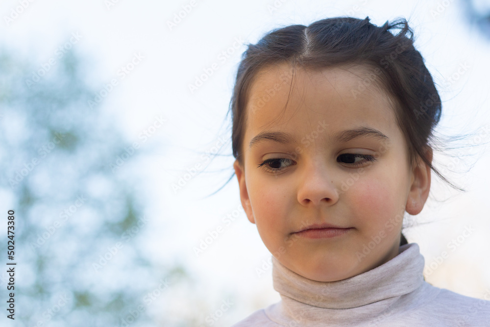 Close-up portrait against the blue sky of a beautiful first-grader girl in a gray turtleneck sweater Close-up portrait against the blue sky of a beautiful first-grader girl in a gray turtleneck sweater