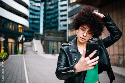 Woman with afro taking a selfie with a smartphone outside in the city