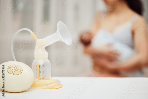 breast pump with breast milk against the background of a mother holding child.