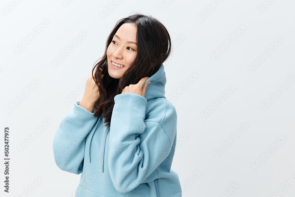 Fashionable smiling happy cute Asian young female in blue sweatshirt puts on the hood posing isolated on over white studio background. The best offer for ad. Fashion New Collection Ad concept Fashionable smiling happy cute Asian young female in blue sweatshirt puts on the hood posing isolated on over white studio background. The best offer for ad. Fashion New Collection Ad concept