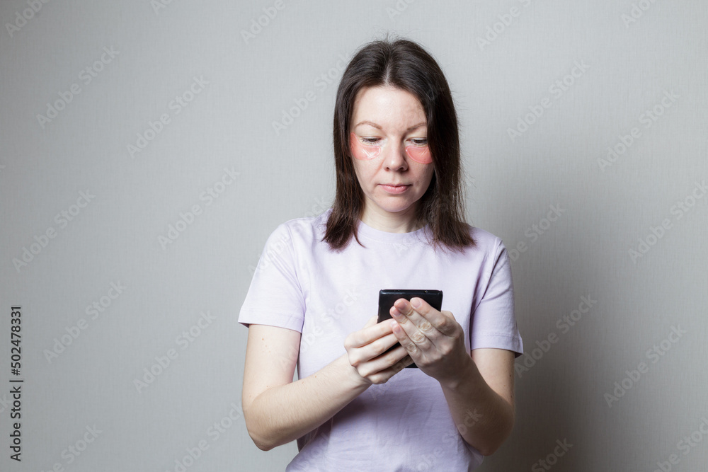 beautiful girl makes a cosmetic procedure. The girl uses eye patches. Skin care under the eyes. woman using phone beautiful girl makes a cosmetic procedure. The girl uses eye patches. Skin care under the eyes. woman using phone